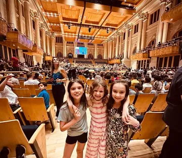 Três crianças estão abraçadas na Sala de Concertos. 