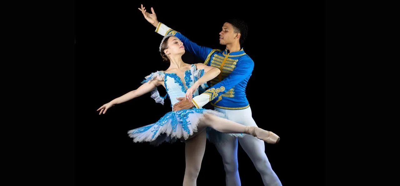 Uma dançarina parada em posição no centro da imagem, demais dançarinos da Cia. Ballet Paraisópolis em volta em movimento