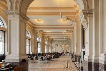 Hall Principal da Sala São Paulo, com paredes em tons de bege e grandes portões metálicos. Ao centro, estão alguns sofás.