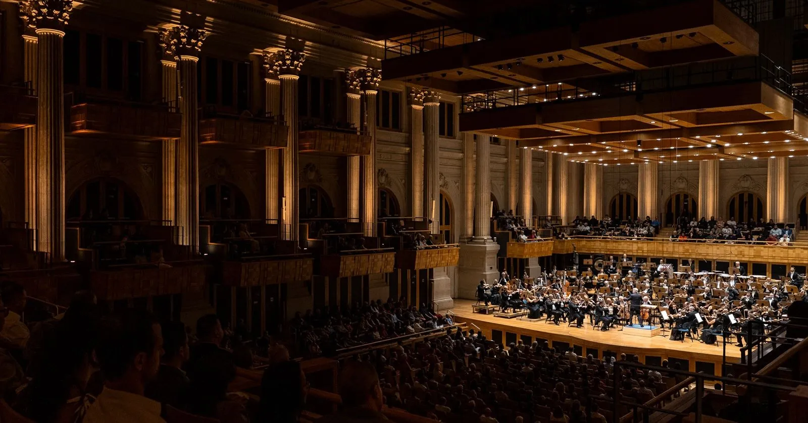 Os músicos da Orquestra estão tocando no palco da Sala São Paulo. Todos estão sentados e com seus instrumentos. A regência é de Thierry Fischer.