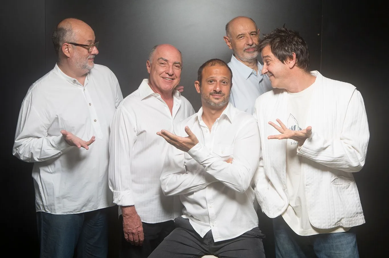 Foto do grupo Pau Brasil, composto por 5 homens adultos. Todos usam camisas brancas e interagem entre si.