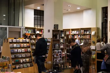 Livros estão dispostos em prateleiras e em cima de uma mesa.