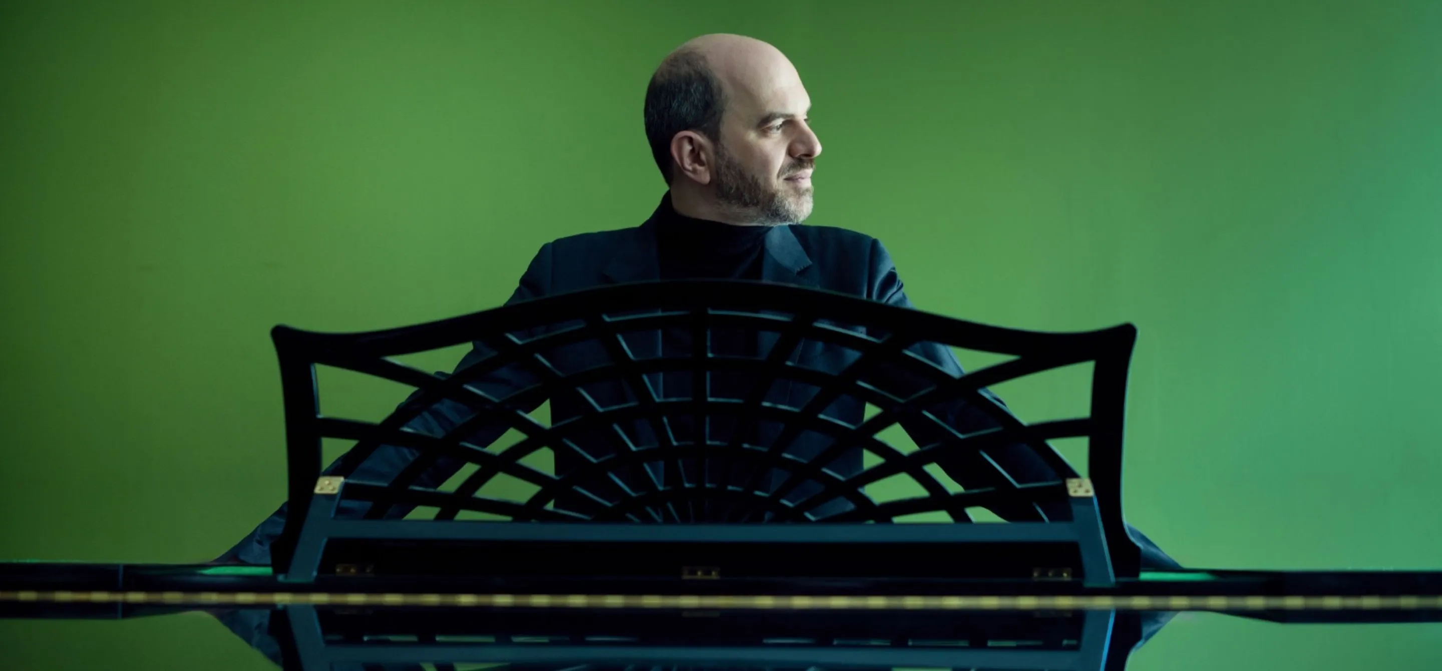 Retrato de Kirill Gernstein, um homem branco e calvo, ao piano com um fundo verde.