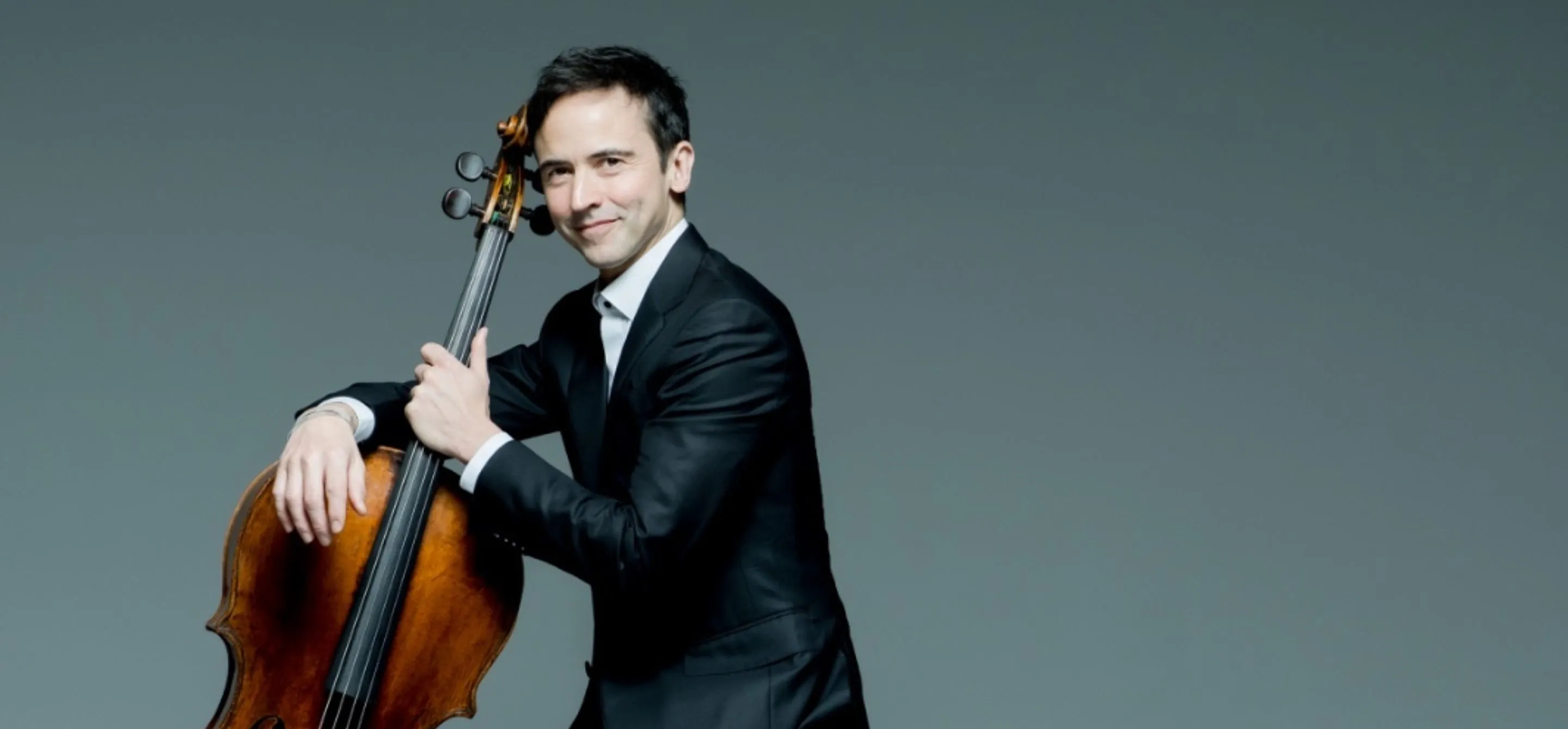 Retrato de Jean-Guihen Queyras, um homem branco de cabelo preto, segurando um violoncelo